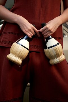 Woman Holding Two Chianti Bottles in Woven Holders at Outdoor Event