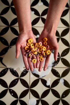 Hands Hold Brightly Colored Cereal on Patterned Floor Tiles