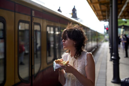 Young Woman Enjoys a Kebab Sandwich at Train Station on Sunny Day