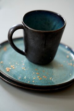 Unique black ceramic mug on a decorative blue plate with crumbs