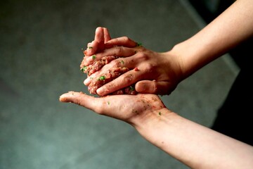 Hands shaping meatball mixture with herbs and spices in a kitchen