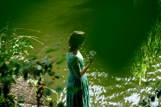 Woman in green dress standing by still water holding a cookie - Powered by Adobe