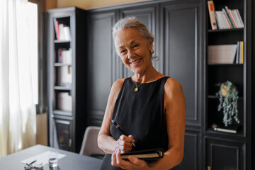 Senior lawyer woman smiling and taking notes in her office