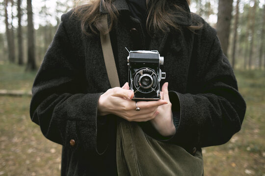 Girl holds vintage medium format camera in serene forest setting