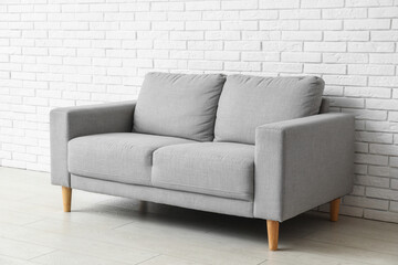 Cozy grey sofa near white brick wall
