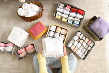 Woman with different clean clothes in organizers sitting on floor