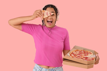 Young African-American woman in headphones with tasty pepperoni pizza on pink background