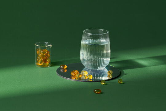 A glass of water with omega-3 capsules on a green background