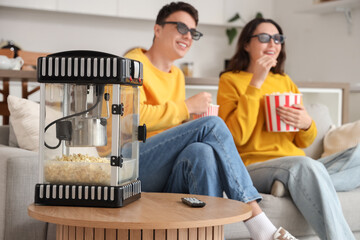 Cute couple watching movie at home, focus on modern popcorn machine