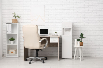 Interior of light office with modern water cooler, workspace and shelving unit