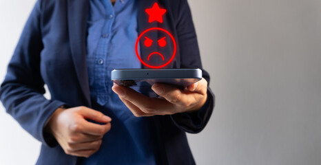 Low rating on satisfaction evaluation. People holding a cell phone with an angry person icon with...