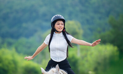 Woman joyfully rides horse in lush green landscape, wearing helmet and casual attire