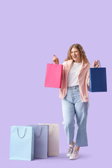 Beautiful young happy woman with shopping bags on purple background
