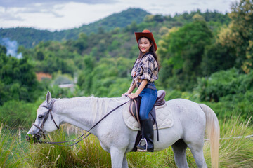 Woman in cowboy hat rides white horse in lush, green landscape, exuding sense of adventure and freedom