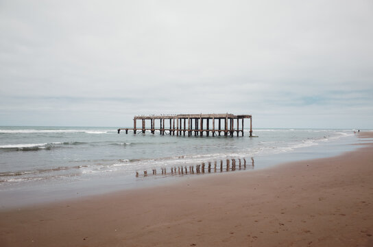Pier Extends Into Calm Water at Cloudy Beach During Midday