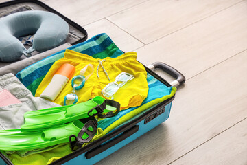 Open suitcase with beach accessories, travel pillow, flippers and bottle of sunscreen cream on floor in living room © Pixel-Shot