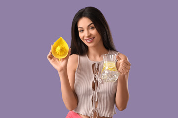 Beautiful young happy woman with jug of infused lemon water and juicer on purple background