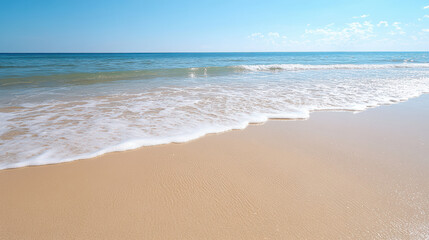 Gentle waves lapping on sandy beach under clear blue sky create serene atmosphere