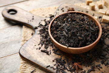 Bowl with dry black tea leaves and star anise on wooden background, closeup