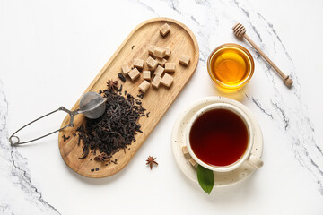 Cup of hot black tea and wooden tray with dry leaves on white background