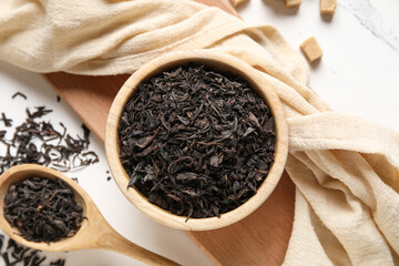 Wooden bowl and spoon with dry black tea leaves on white background