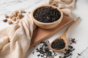 Wooden bowl and spoon with dry black tea leaves on white background, closeup