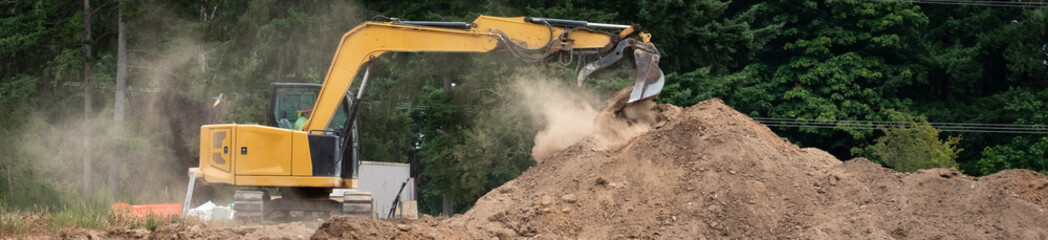 Earthworks phase of new home construction project, excavator digging up dirt, and producing dust,...
