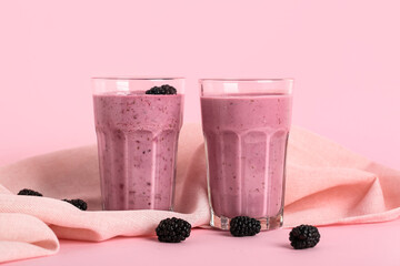 Glasses of fresh blackberry smoothie and berries on pink background