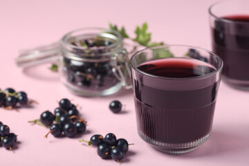 Glasses of fresh black currant juice and jar with berries on pink background, closeup