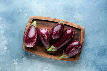 Wooden board with fresh ripe eggplants on light blue background