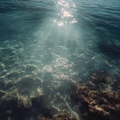 Fototapeta premium Sunbeams illuminating shallow coastal waters, rocks visible underwater, peaceful seascape, summer vacation background