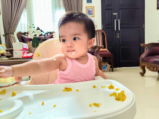 happy infant asian baby girl excited eating food on a chair. 