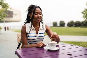 Young student stirring cappuccino at outdoor cafe table
