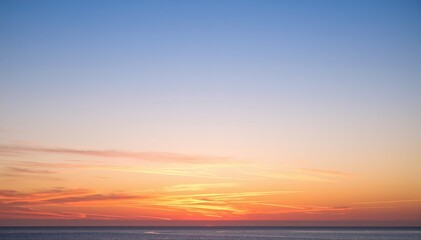 Fototapeta premium A serene boat glides across the shimmering water, silhouetted against a vibrant sunset, with hues of orange, pink, and purple reflecting on the waves.