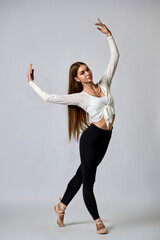 A woman in a white shirt and black pants is dancing with her arms outstretched