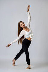 A woman in a white shirt and black pants is dancing with her arms outstretched