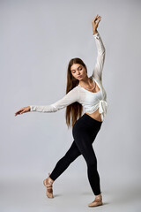 A woman in a white shirt and black pants is dancing with her arms outstretched