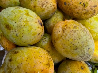 Close up shows a heap of ripe yellowish mangoes with scattered brown spots and blemishes