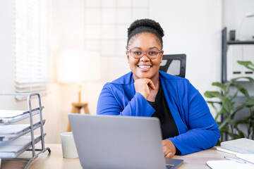 Smiling african american businesswoman in blue blazer working on laptop at office desk.