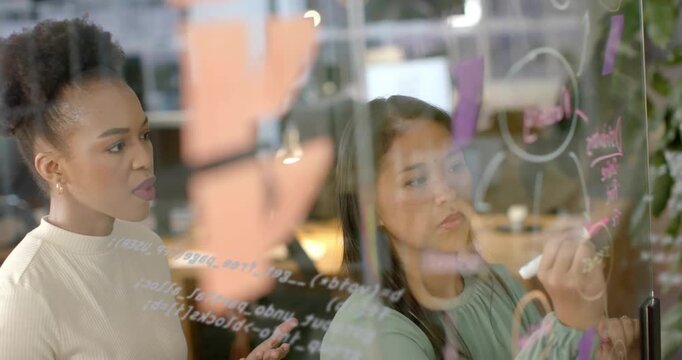 Coworkers reaching for markers initiating flowchart brainstorming on glass board in business office