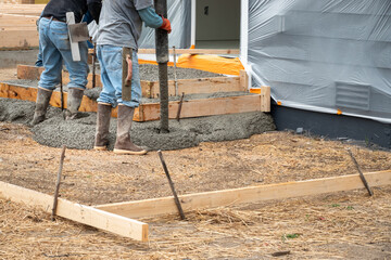 Construction workers in rubber boots and hard hats working cement pumper hose to pour fresh cement...