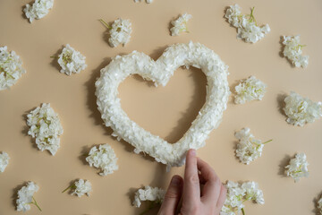 Hand holding Symbol of love beautiful flower petals in heart shape in beige background. Creative concept of St Valentines day, weeding romantic date or anniversary. Copy space greeting card