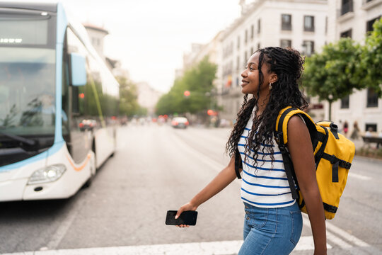 Young black woman crossing the street holding a smartphone