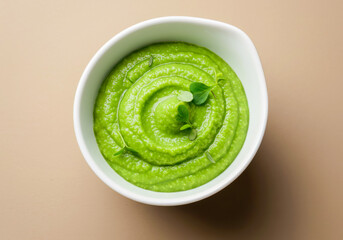 Obraz premium Top-down view of a bright green edamame puree or dip, artfully swirled and garnished in a white serving bowl.