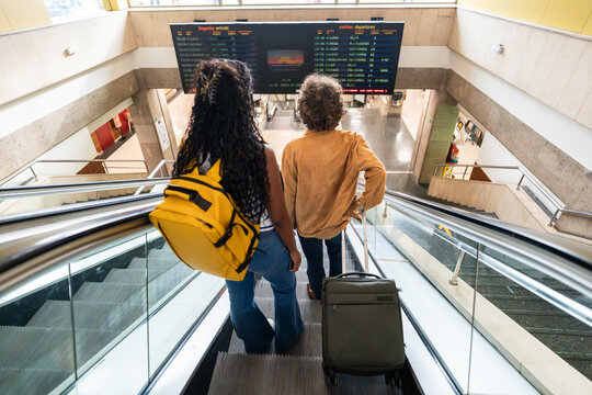 Tourists going up escalator looking at timetable screen in airport