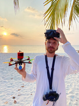 Man holding FPV drone at sunset beach