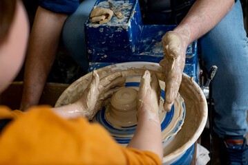 Faceless Master and a child make a clay plate on a potter's wheel