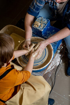 Faceless Master and a child make a clay plate on a potter's wheel