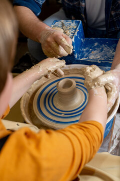 Faceless Master and a child make a clay plate on a potter's wheel