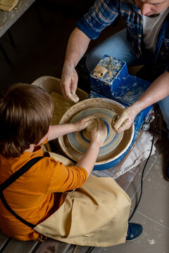 Master and a child make a clay plate on a potter's wheel